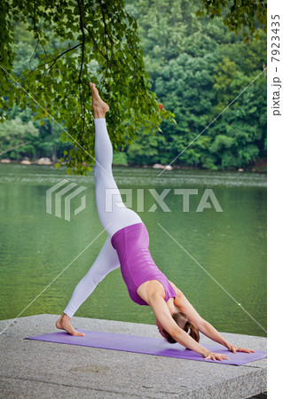 Mid adult woman performing yoga downward dog split pose by river Mid adult woman performing yoga downward dog split pose by river 7923435