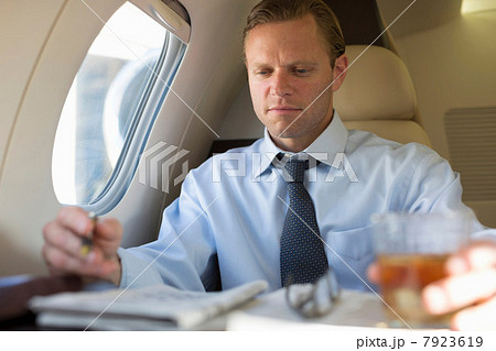 Businessman doing crossword on airplane Businessman doing crossword on airplane 7923619
