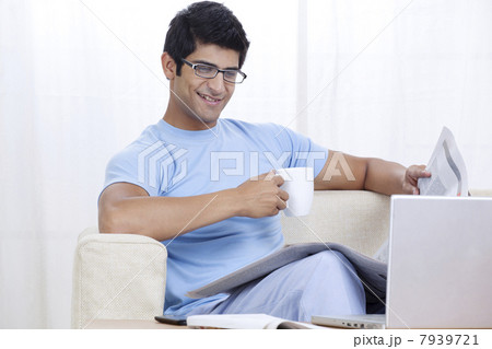 Young man enjoying cup of coffee at home while looking at laptop 7939721