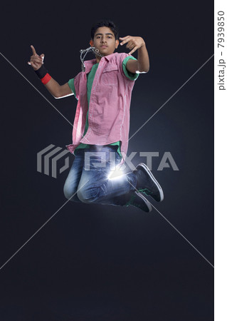 Funky teenage boy jumping in air showing rock and roll sign against black background 7939850