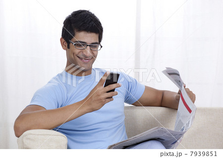 Happy young man looking at mobile phone while sitting on sofa 7939851