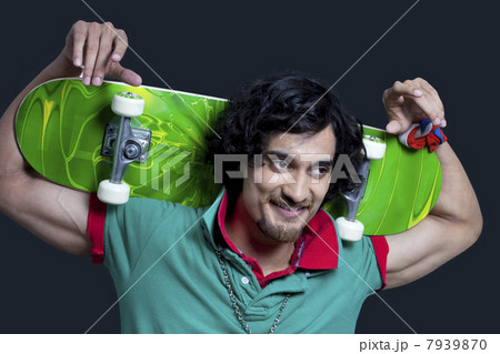 Close-up of young smiling man holding skateboard behind head against black background Close-up of young smiling man holding skateboard behind head against black background 7939870