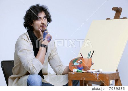 Young male artist contemplating near easel against colored background 7939886