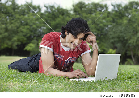 Smiling young man lying on grass using laptop 7939888