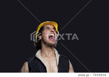 Close-up of young man with hardhat shouting against black background 7939916
