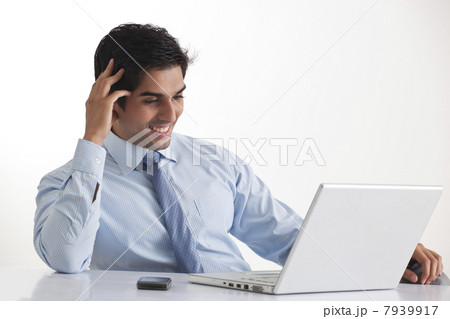 Happy young male executive smiling while looking at laptop 7939917