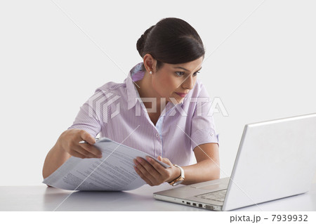 Businesswoman with paperwork looking at laptop screen Businesswoman with paperwork looking at laptop screen 7939932