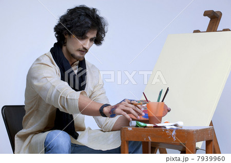 Young artist sitting near easel against colored background Young artist sitting near easel against colored background 7939960