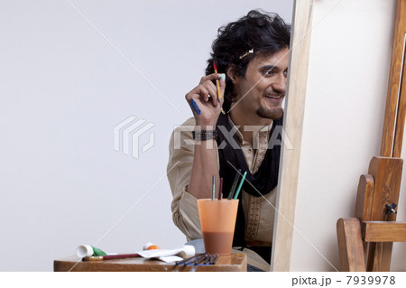 Smiling young male artist holding paintbrush against colored background 7939978