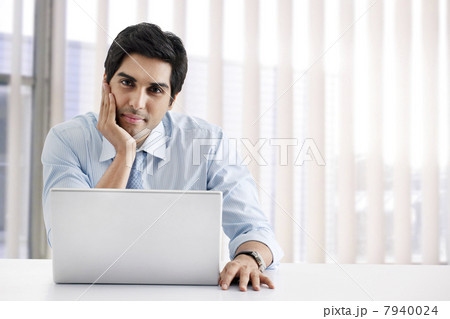 Happy young businessman sitting at his desk with laptop 7940024