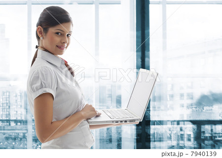 Portrait of young businesswoman smiling with laptop at office Portrait of young businesswoman smiling with laptop at office 7940139
