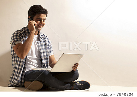 man looking at laptop screen while using cell phone 7940204