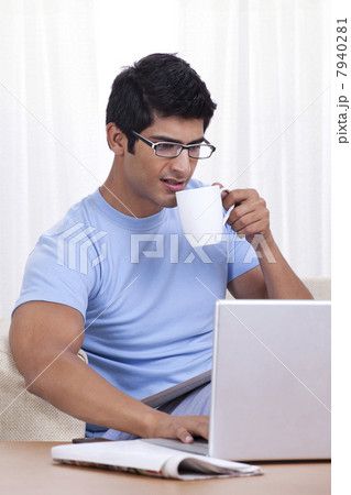 Young man taking a sip of coffee while operating laptop 7940281