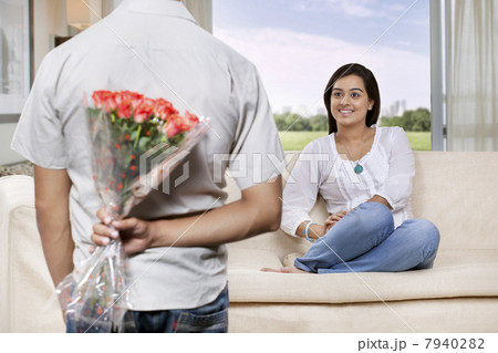 Man hiding bunch of flowers behind back while woman watching 7940282