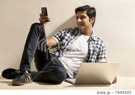 Happy relaxed young man sitting by laptop while reading text message 7940305