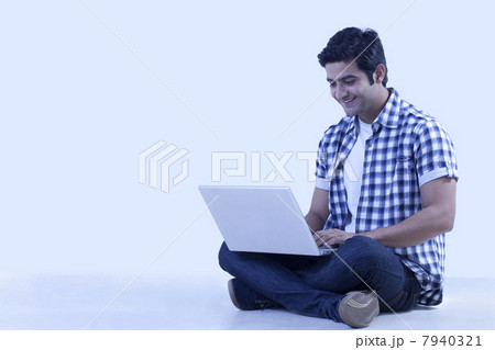 Smiling young man sitting on floor with laptop 7940321