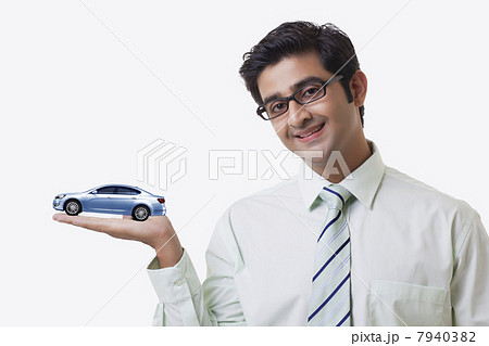 Smiling male sales executive holding car model over white background 7940382