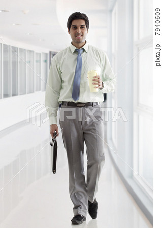 Businessman with bag and coffee cup walking in office corridor 7940609