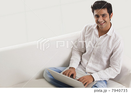 Casually dressed young man on sofa using laptop at home 7940735