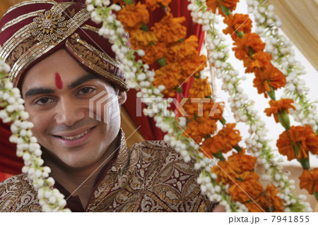 Close-up of smiling young Indian bridegroom behind wreath 7941855