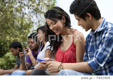 Young friends using cell phone with people in the background 7942008