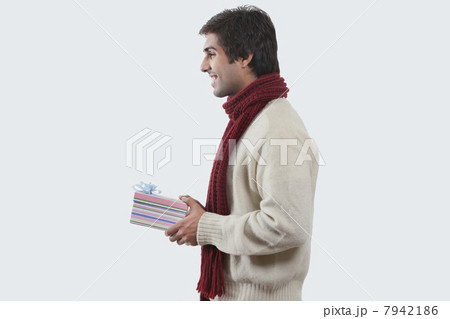Smiling young man holding gift box over colored background 7942186
