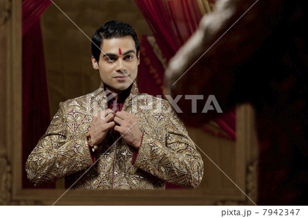 Bridegroom looking at self in mirror while getting dressed for wedding 7942347