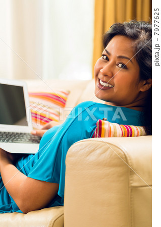 Asian Woman sitting on couch surfing the internet and smiling 7977625