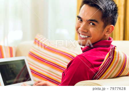 Asian man sitting on couch surfing the internet 7977628