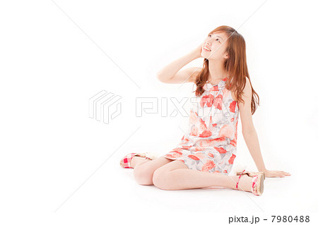 ワンピースを着て座って斜め上を見上げる若い女子の写真素材