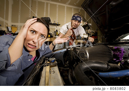Frustrated woman with incompetent mechanic in background 8083802