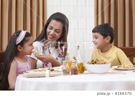 Cheerful mother feeding her daughter pizza with son sitting besides Cheerful mother feeding her daughter pizza with son sitting besides 8166370