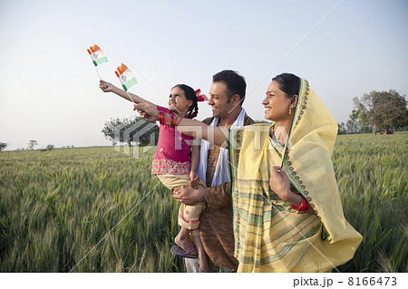 Rural family standing in the field holding Indian flag 8166473