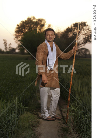 Full length of an Indian farmer standing with a stick 8166543