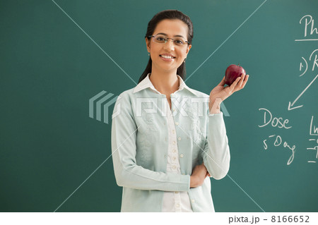 Portrait of young elementary school teacher holding an apple against green board Portrait of young elementary school teacher holding an apple against green board 8166652