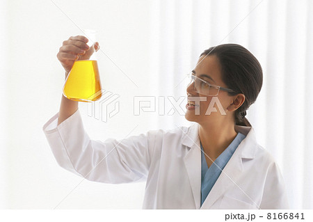 Young female scientist looking at yellow liquid in beaker Young female scientist looking at yellow liquid in beaker 8166841
