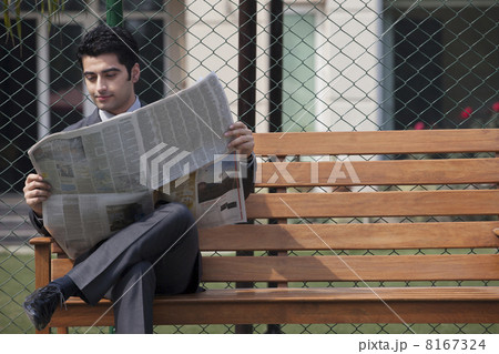Young male business corporate executive reading newspaper while sitting on bench in tennis court 8167324