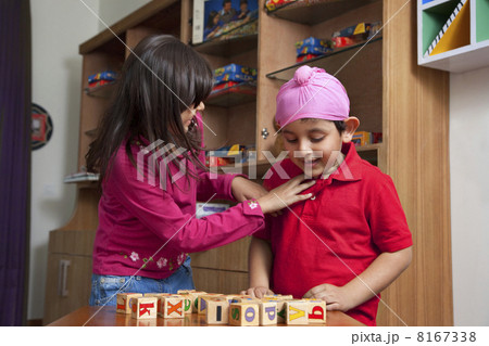 Little boy looking at wooden toy blocks while standing with sister 8167338
