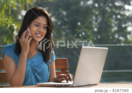 Young woman answering phone call while working on laptop 8167560