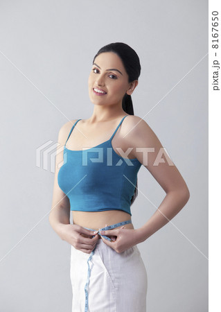Portrait of young woman measuring waist isolated over gray background 8167650