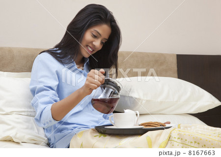 Young woman pouring tea in cup while sitting on bed 8167663
