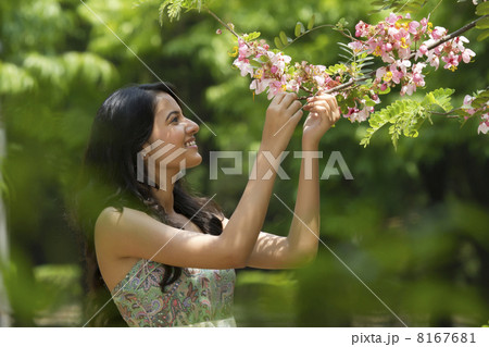 Young woman looking at flowers on a branch Young woman looking at flowers on a branch 8167681
