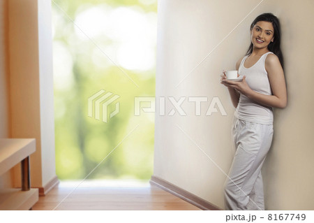 Portrait of beautiful young woman leaning on wall while holding cup of coffee 8167749