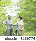 新緑の中で自転車を押すシニア夫婦 8169776