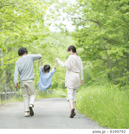 新緑の中で手をつなぐ家族の後姿の写真素材