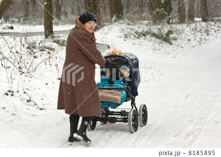 Great-grandmother walking with baby boy in pram during snowfall 8185895