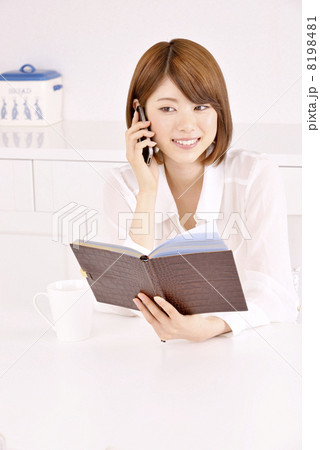 手帳を見ながら電話をする女性 8198481