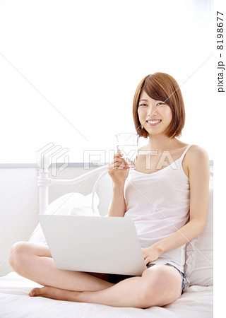 ベットの上でパソコンをしながら水を飲む女性 ベットの上でパソコンをしながら水を飲む女性 8198677