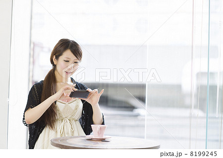 窓辺でスマートフォンで写真を撮る若い女性 8199245