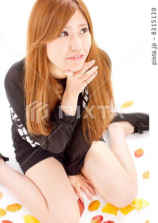 落ち葉の上に座って楽しそうに何かを考える20代の可愛い女の子 8315139